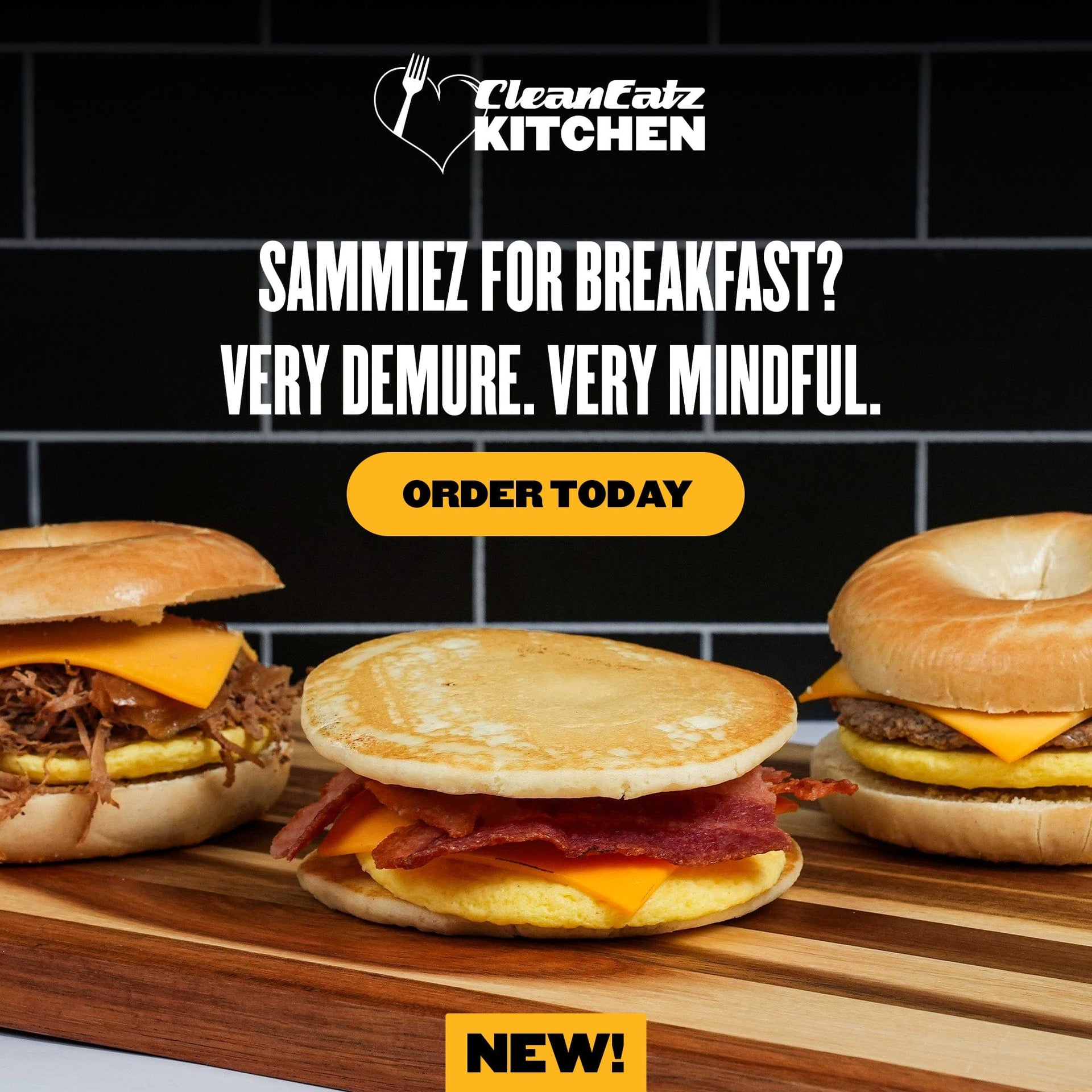  A promotional Clean Eatz Kitchen image showcasing three Breakfast Sammiez sandwiches on a wooden board. The sandwiches include a pulled meat and cheese bagel, a bacon, egg, and cheese pancake sandwich, and a sausage, egg, and cheese bagel. The ad copy reads: "Sammiez for breakfast? Very demure. Very mindful." with a yellow "Order Today" button and "NEW!" tag at the bottom.