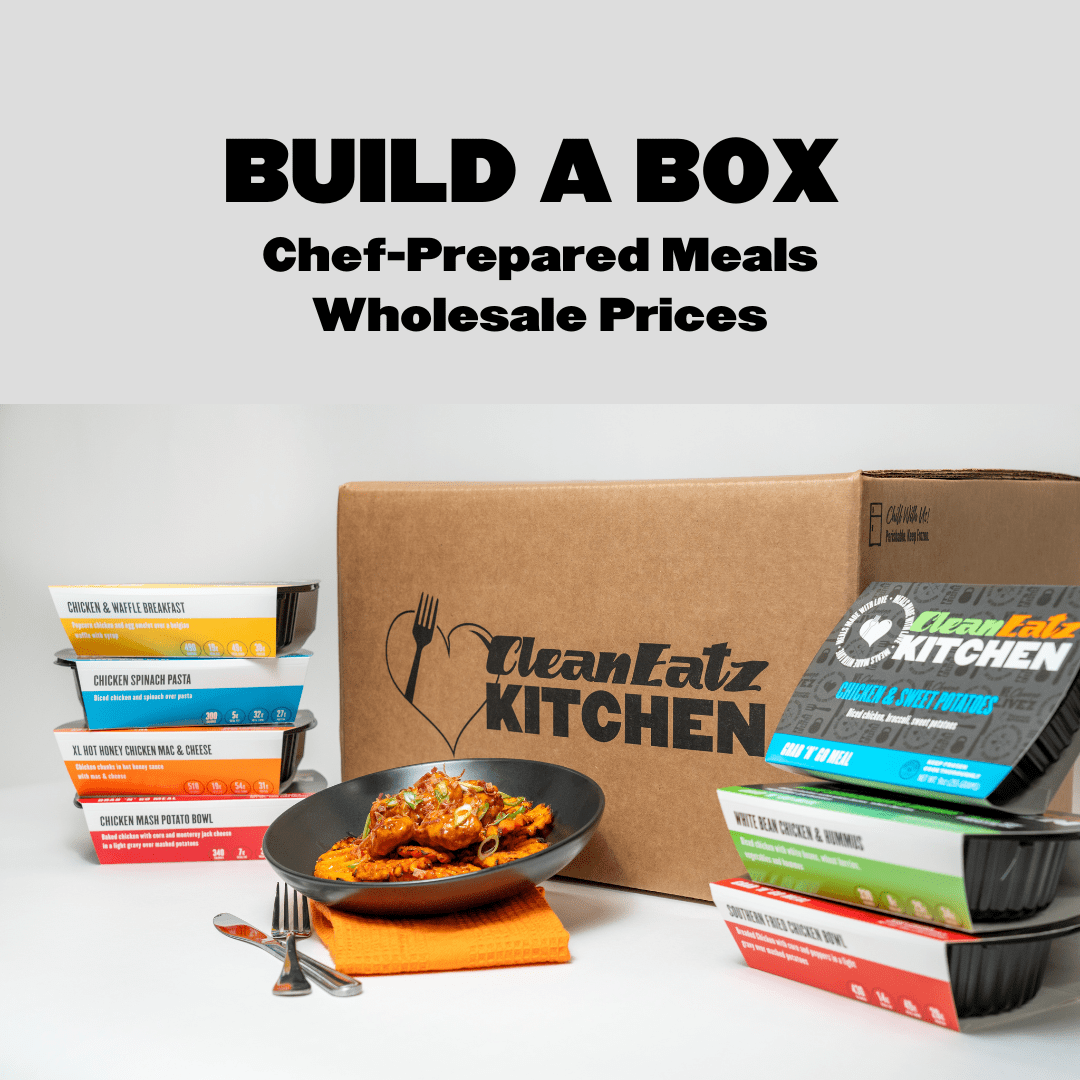 A promotional image for Clean Eatz Kitchen's 'Build a Box' meal plan, featuring a branded cardboard box, chef-prepared meal trays stacked on both sides, and a plated meal in the foreground. The text 'BUILD A BOX - Chef-Prepared Meals, Wholesale Prices' is prominently displayed at the top. The meals have colorful labels indicating different flavors and meal types.