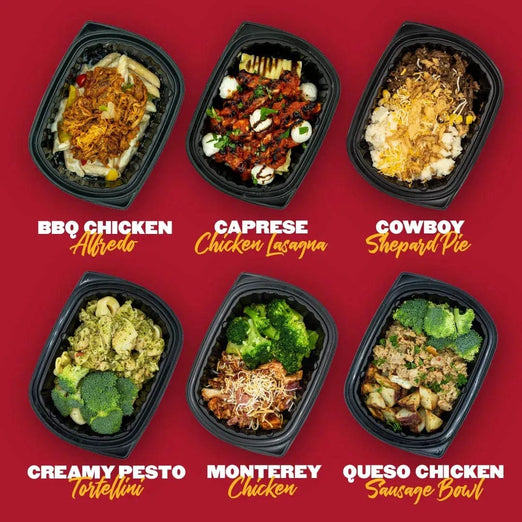 Six Clean Eatz Kitchen meals in black meal containers, displayed against a red background. The meals include BBQ Chicken Alfredo, Caprese Chicken Lasagna, Cowboy Shepherd's Pie, Creamy Pesto Tortellini, Monterey Chicken, and Queso Chicken Sausage Bowl. Each dish features vibrant and appetizing ingredients like pasta, cheese, vegetables, and proteins.